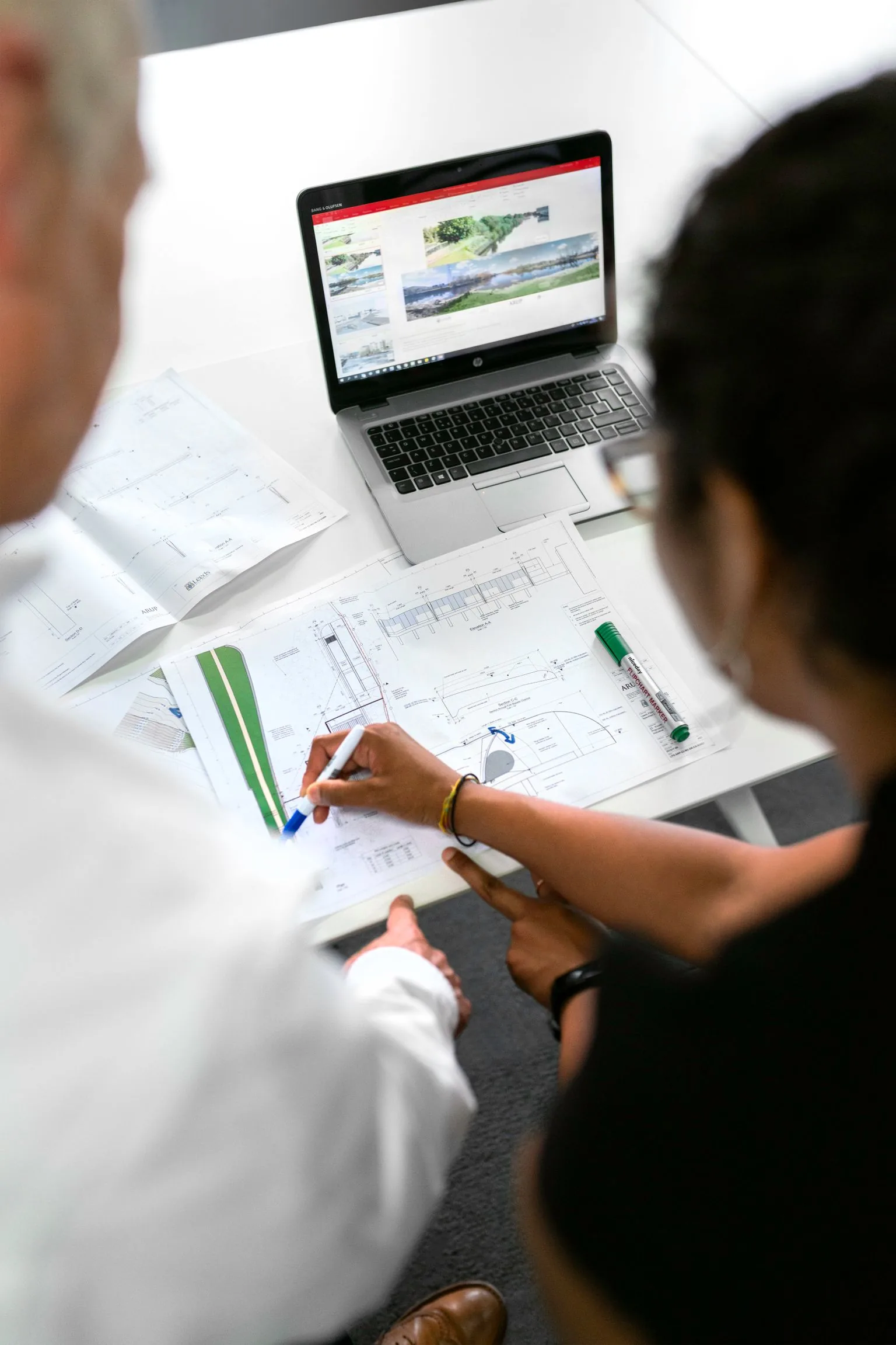 Two engineering collaborators reviewing technical drawings and a laptop together